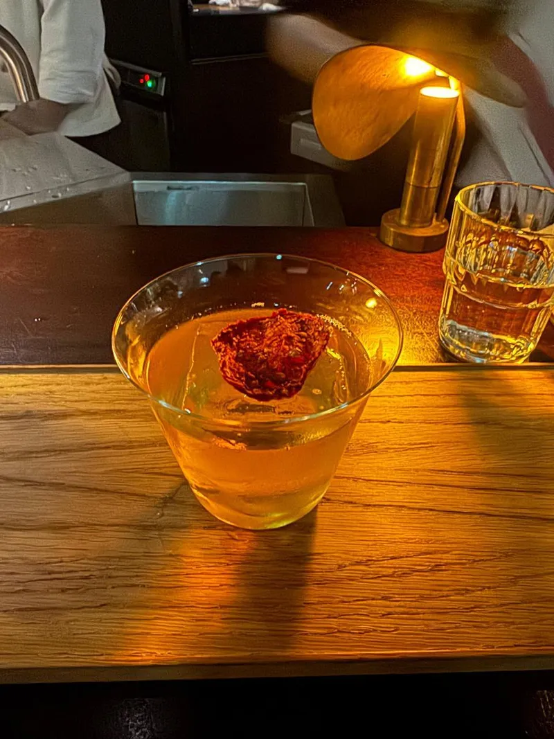 木質吧台上的 Kyoto Bloody Mary，清澈酒液上放著番茄裝飾，旁邊是暖色桌燈